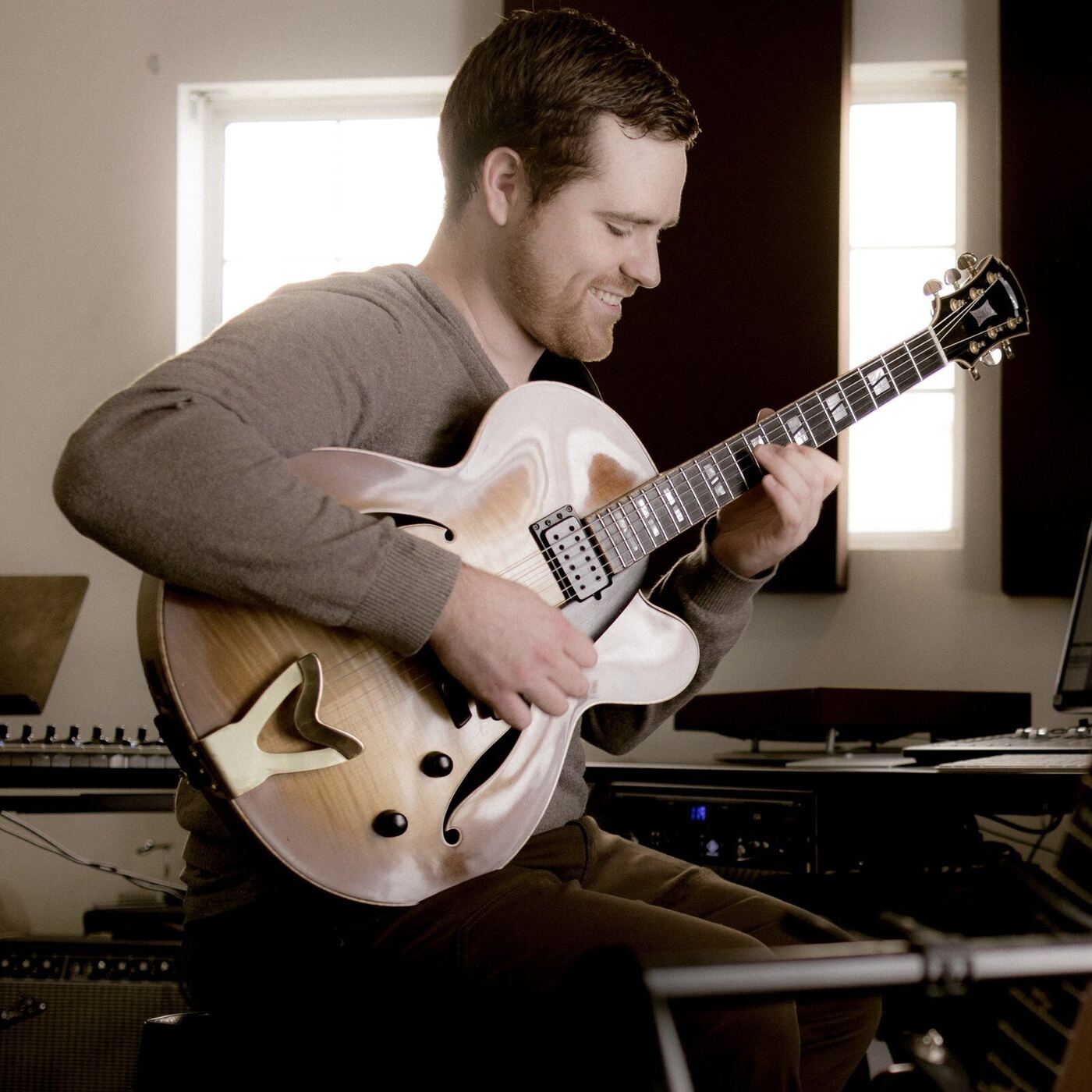 Ryan smiling, playing an archtop guitar in the studio