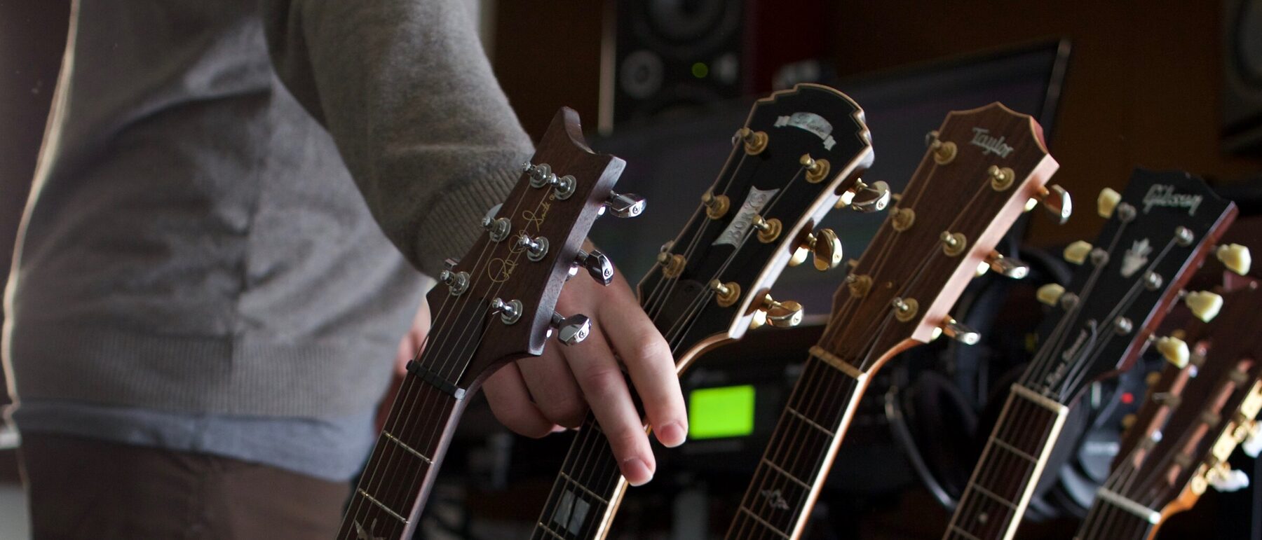 Ryan reaching for one of his studio guitars, with a rack of other instruments