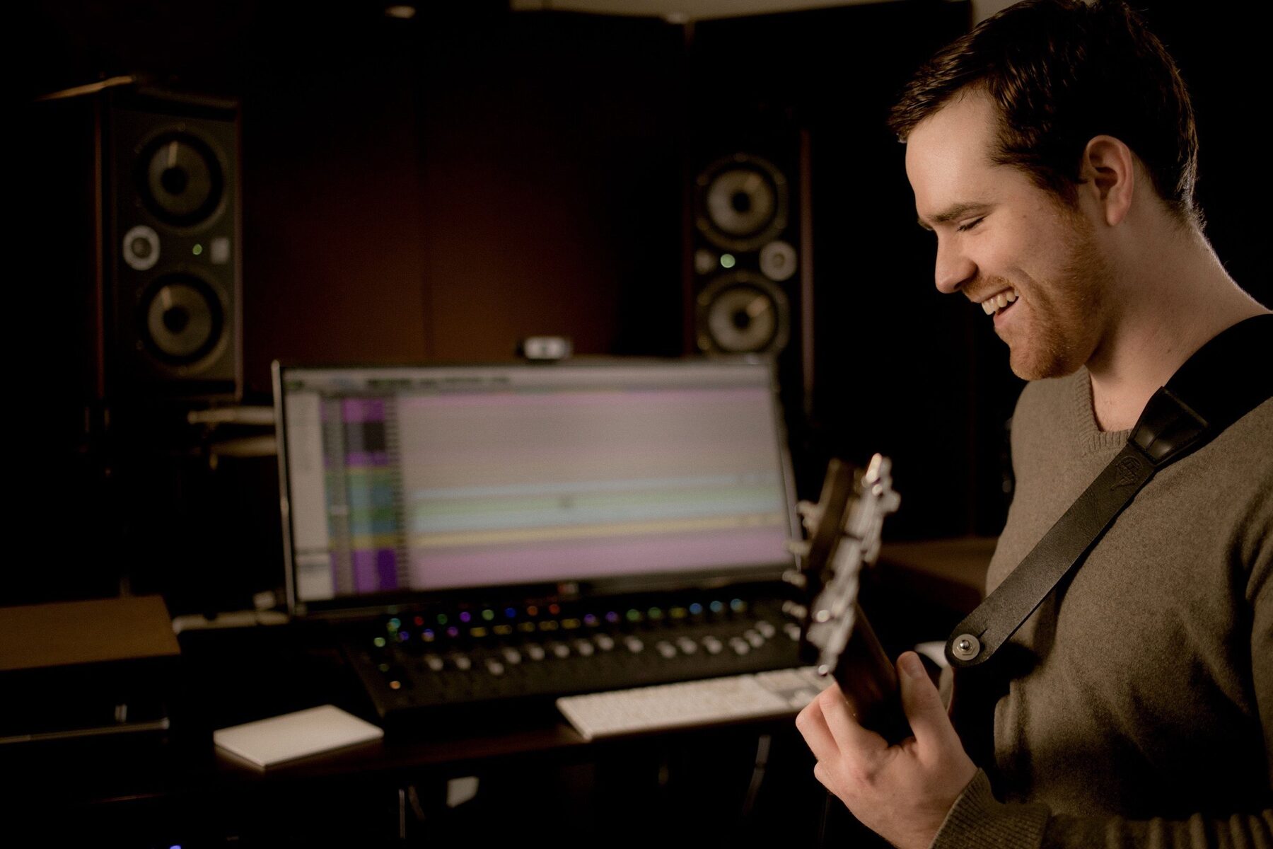 Ryan smiling, playing guitar at the studio console